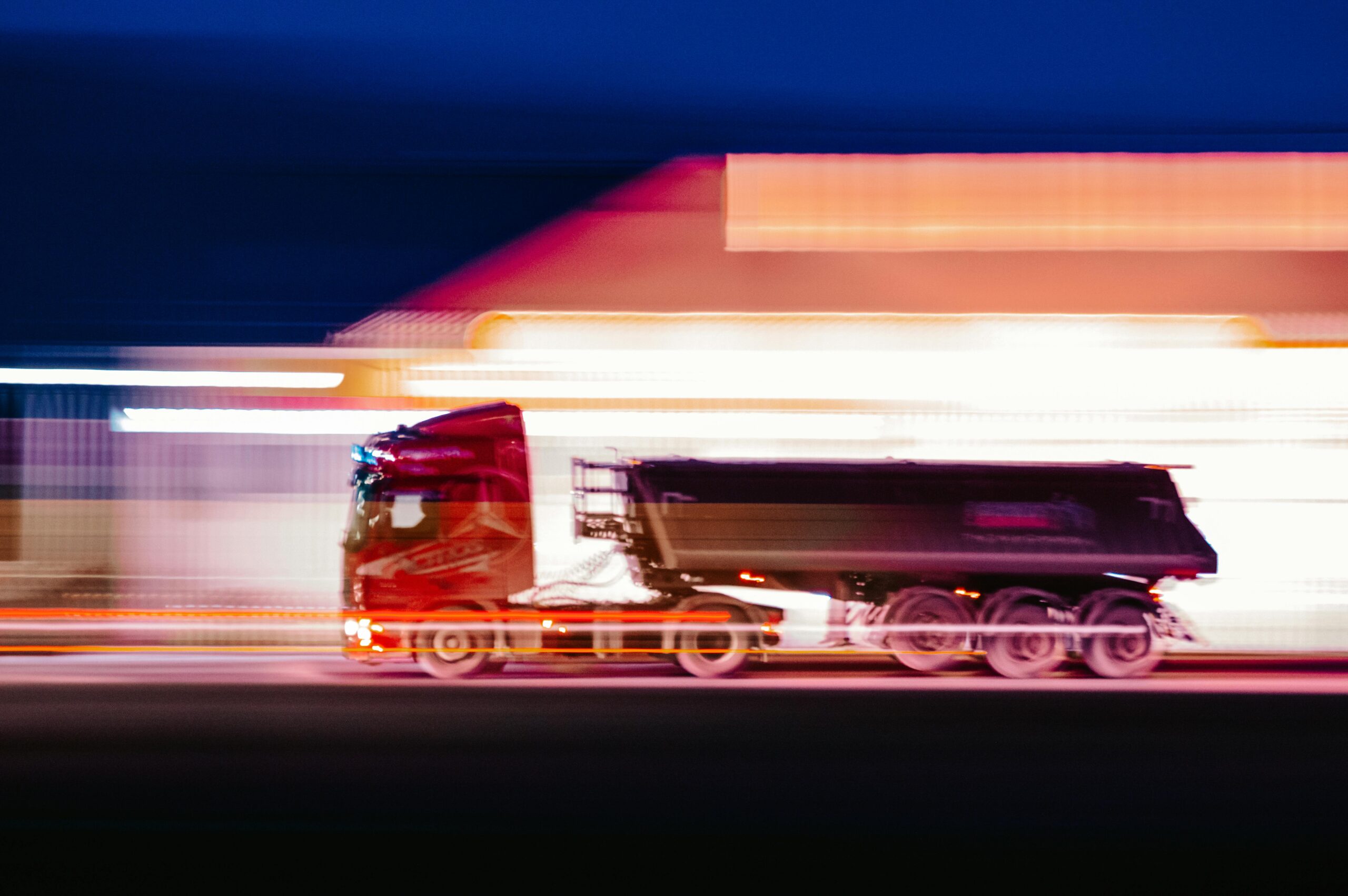 A vibrant motion blur photo of a truck speeding through city streets at night.