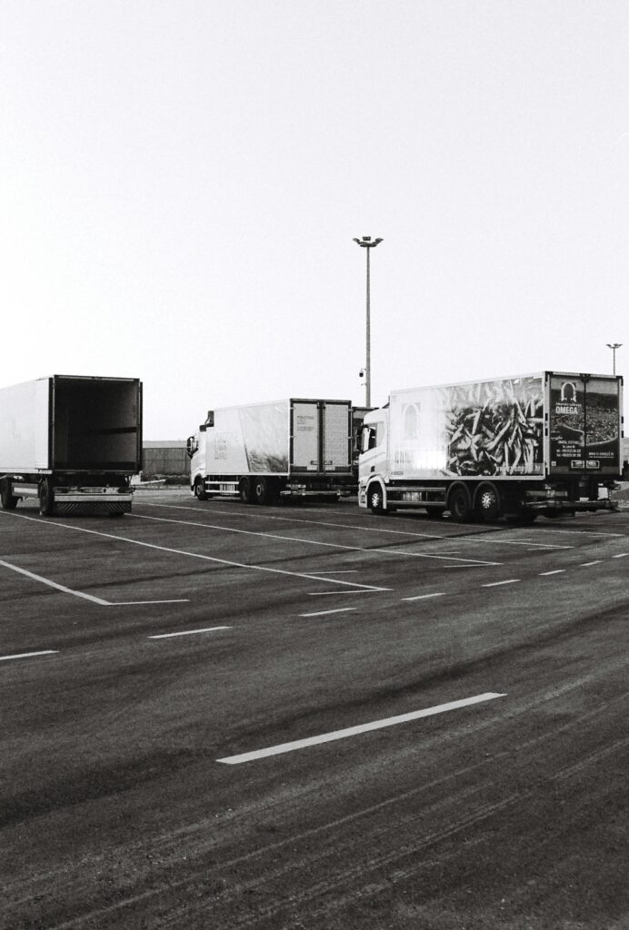 Black and white photo of multiple trucks parked in an empty urban parking lot, taken during the day.